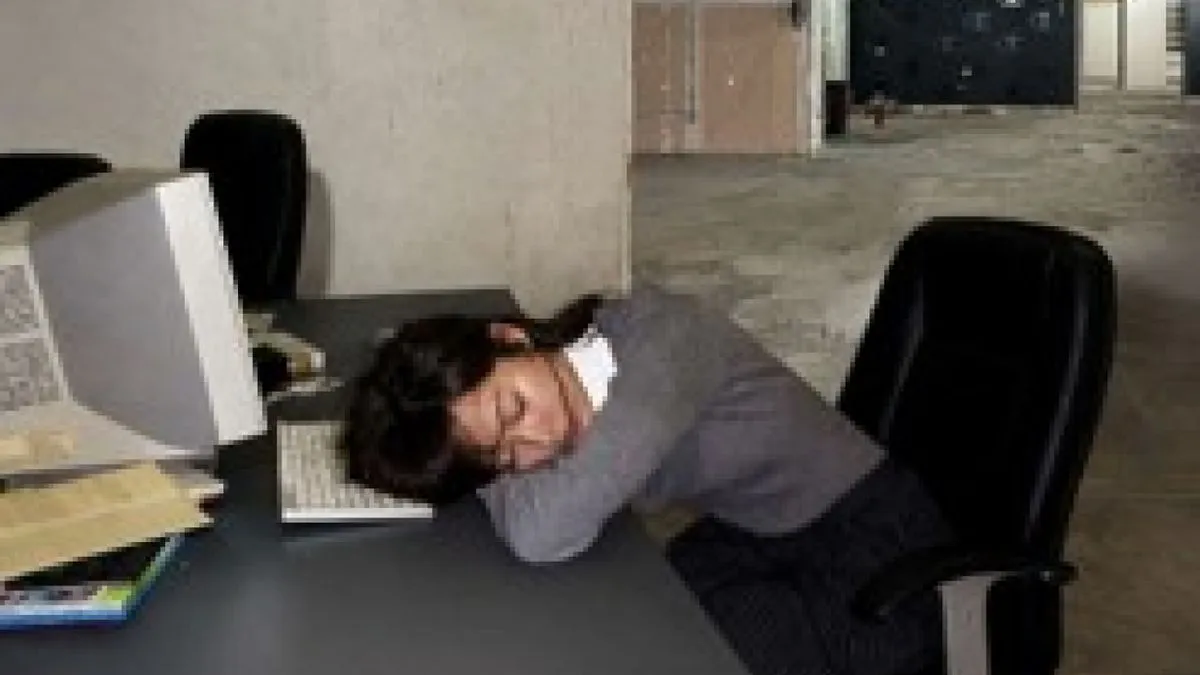 Grainy image of a woman sleeping at a generic office desk